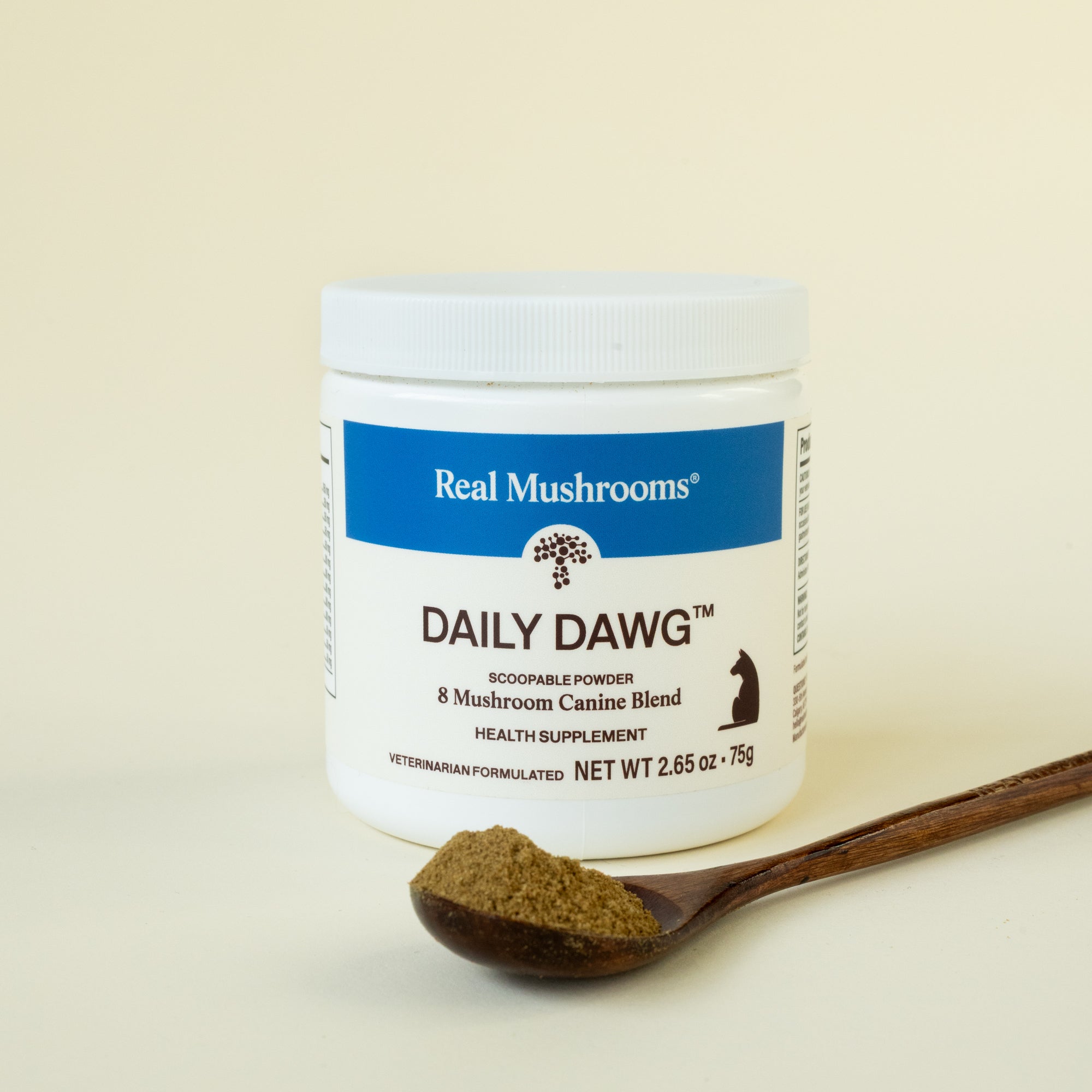 A jar of Real Mushrooms Daily Dawg™ Powder for Pets sits beside a wooden spoon filled with the scoopable canine wellness supplement.