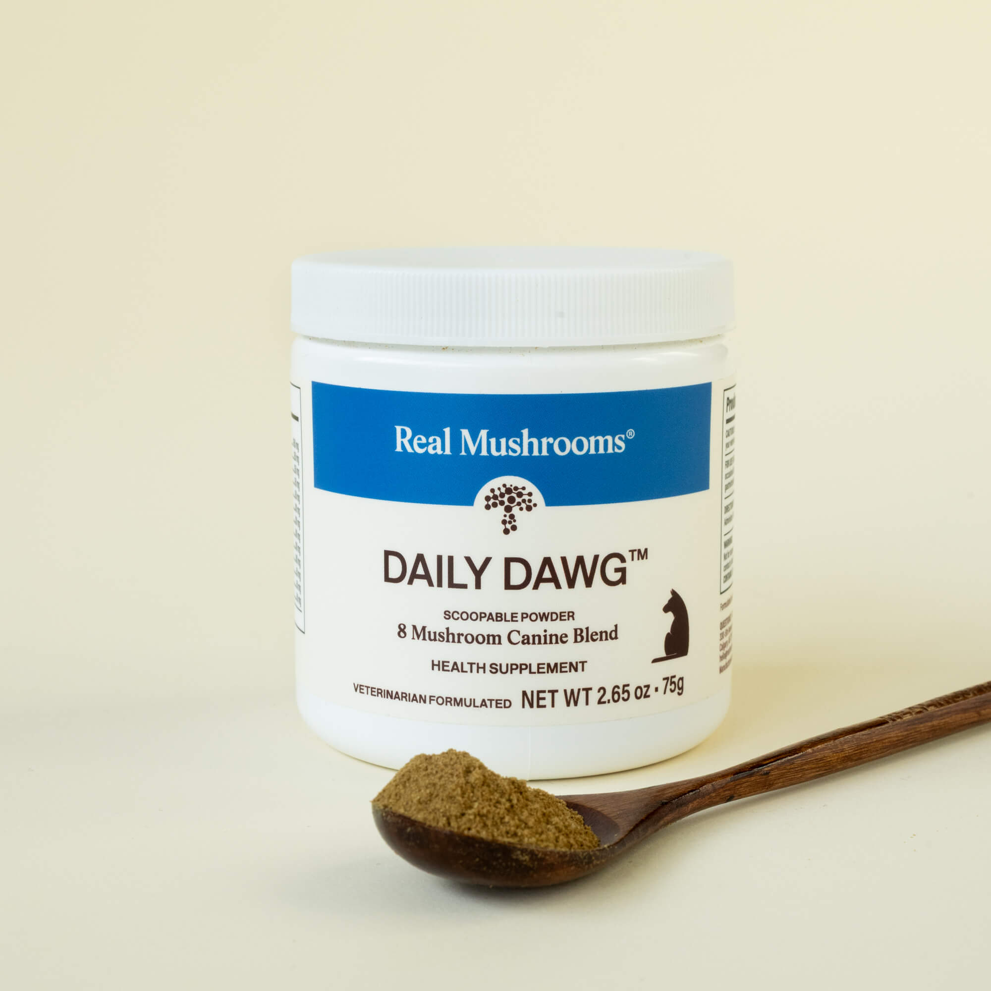 A white container of Real Mushrooms Daily Dawg™ Powder for Pets, a dog wellness supplement, is shown next to a wooden spoon filled with organic mushroom powder.