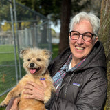 Joni Kamlet holding a small dog outdoors next to a tree