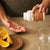 A person pours Organic Cordyceps-M® Extract Capsules by Real Mushrooms into their hand, showcasing energy support benefits beside orange slices and a glass of water on a table.