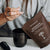 Someone scoops Real Mushrooms Mushroom Hot Chocolate Mix from a brown packet into a black mug, preparing a cozy vegan hot chocolate.