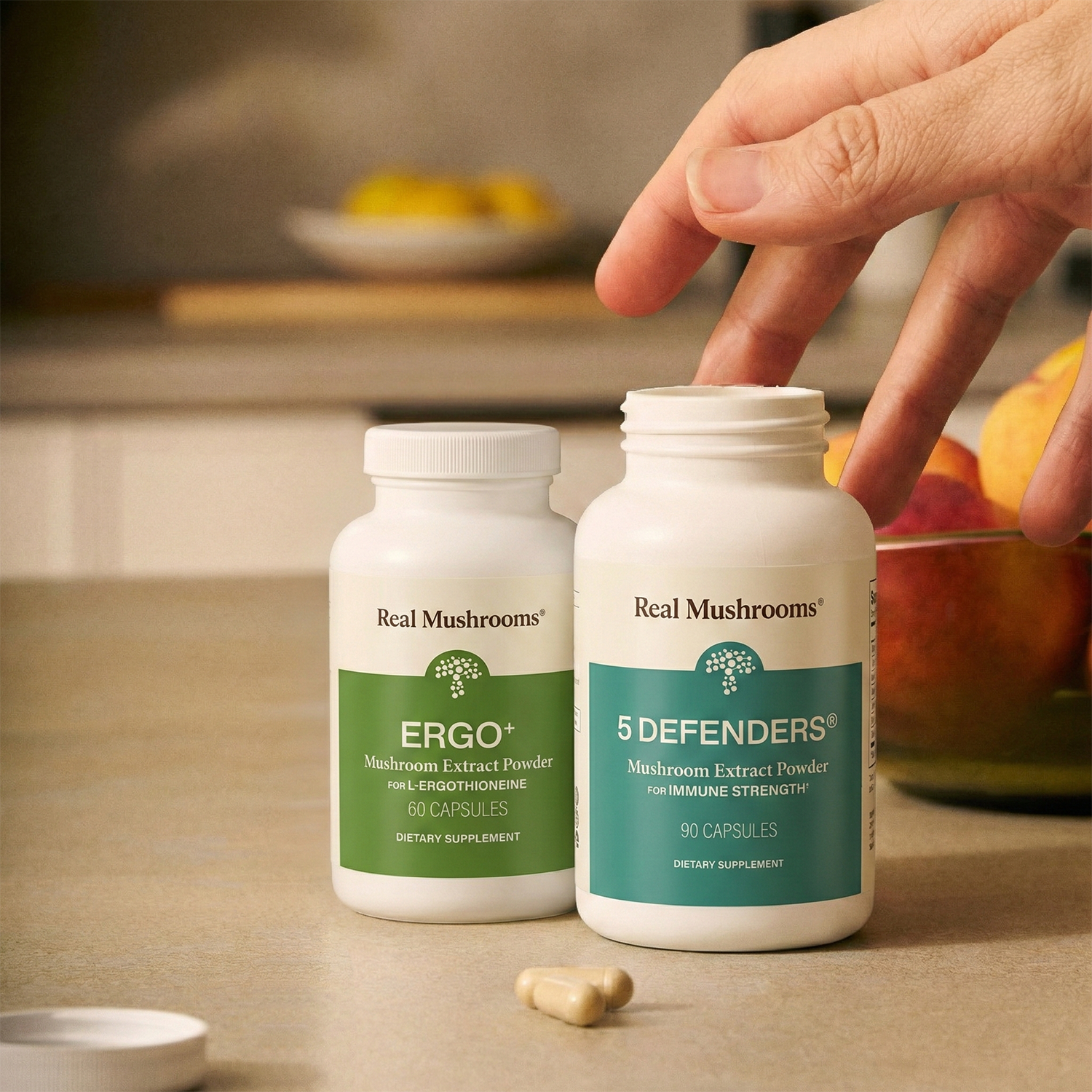 Two bottles of Real Mushrooms Immune Power supplements sit on a counter with capsules next to them, showcasing the strength of mushroom-based immune support as a hand reaches for a bottle.
