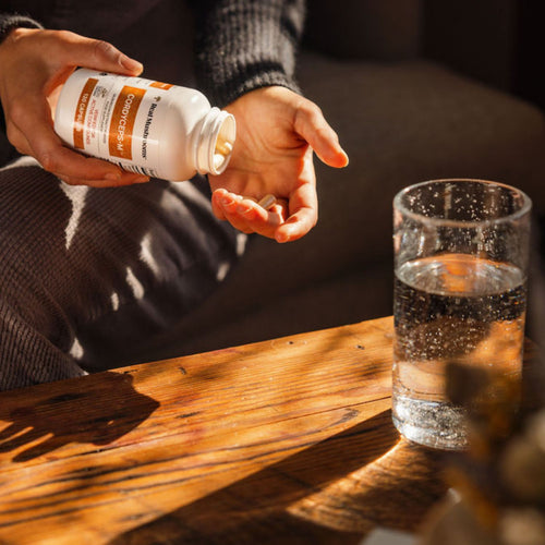 Someone pours Real Mushrooms Organic Cordyceps Extract Capsules from the bottle into their hand, with a glass of water on a wooden table nearby, ready to support natural energy.