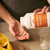 Someone pours Real Mushrooms Organic Cordyceps-M® Extract Capsules into their hand next to orange slices and a glass of water, emphasizing natural energy support.
