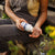 Outdoors, a person pours Real Mushrooms Mushroom D2Z immune support capsules from a white bottle into their hand, with a glass of water and plants nearby.