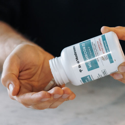 A person pours capsules from a Real Mushrooms Vitamin D from Organic Mushrooms bottle into their hand.