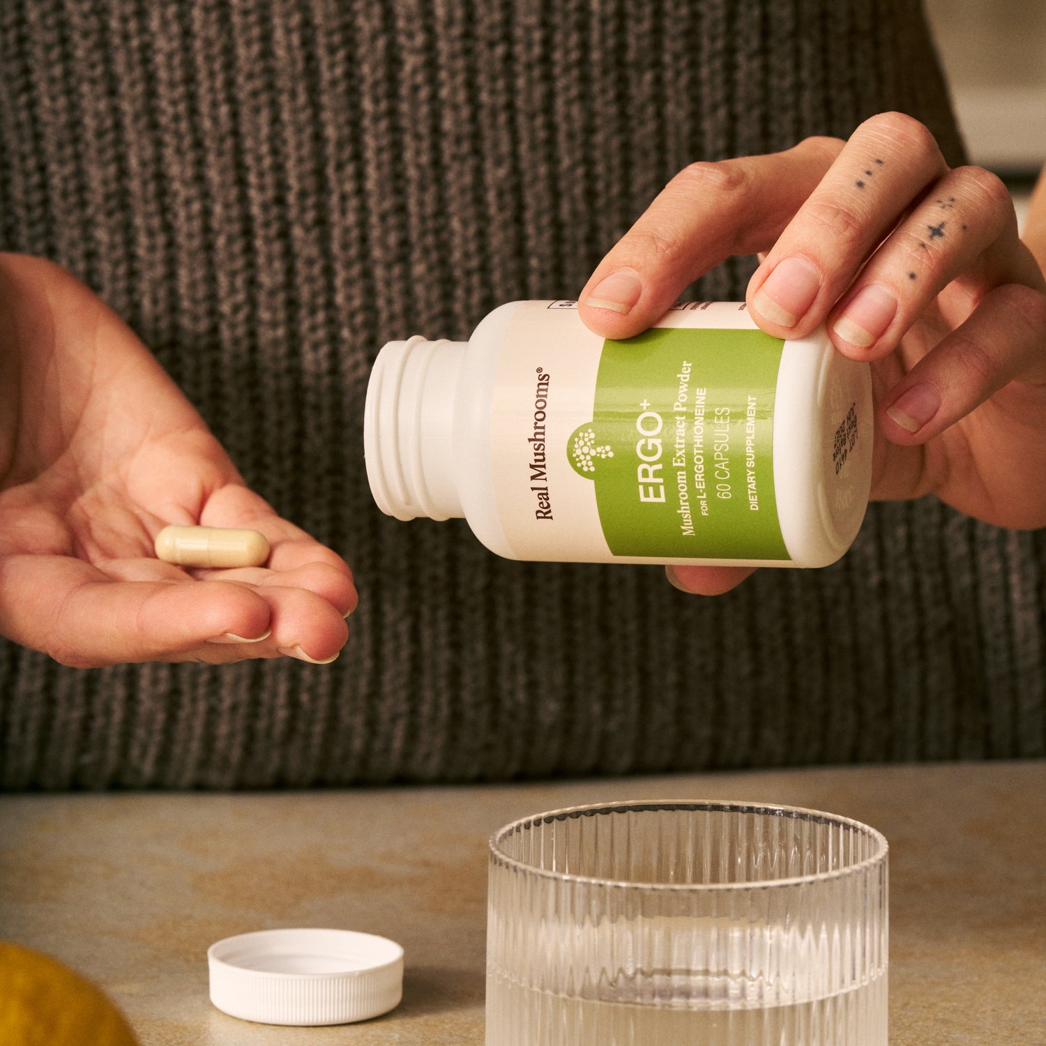 A person holding a Real Mushrooms Ergo+ Ergothioneine Supplement pill, an antioxidant supplement derived from golden oyster mushrooms.