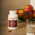 A bottle of Real Mushrooms Organic Reishi Mushroom Capsules is displayed on a countertop beside two capsules, a glass of water, and a bowl of peaches.