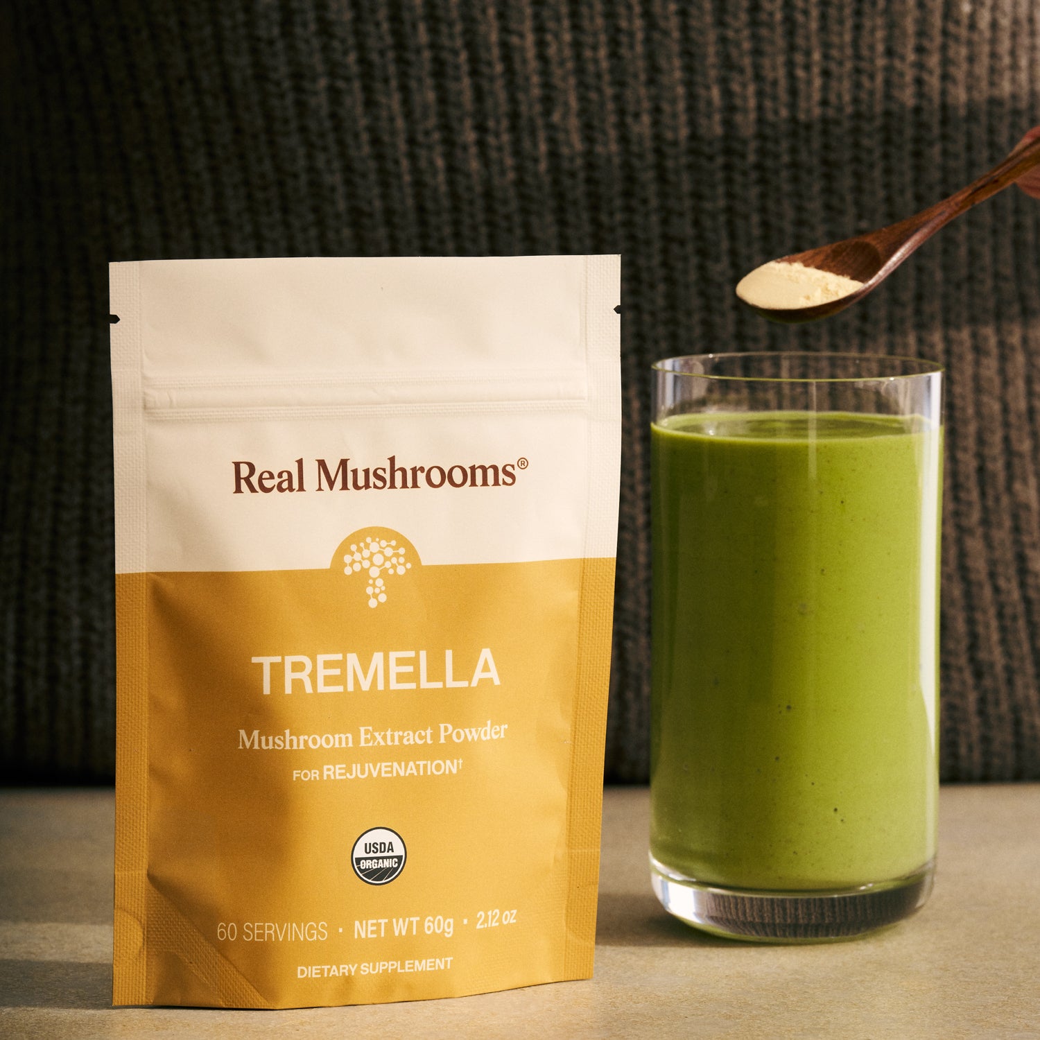 A bag of Real Mushrooms Organic Tremella Extract Powder is placed by a green smoothie, as a spoonful of the powder is added to the drink to support skin, hair, and nail health.