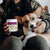 A person holding a container of Real Mushrooms Mushroom Mobility Pet Chews, a hip and joint supplement for pets, sits with their corgi on their lap.