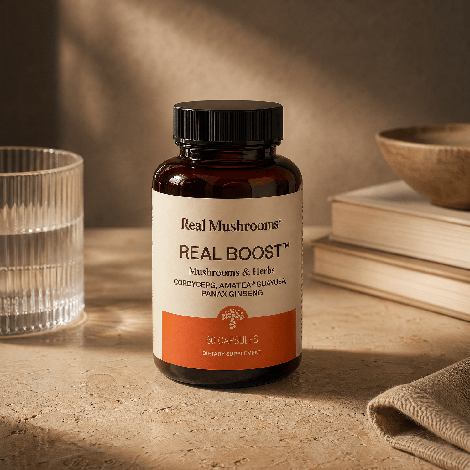A bottle of Real Mushrooms RealBoost—Cordyceps, Guayusa, and Ginseng—rested on a textured surface beside a glass of water and a stack of books.