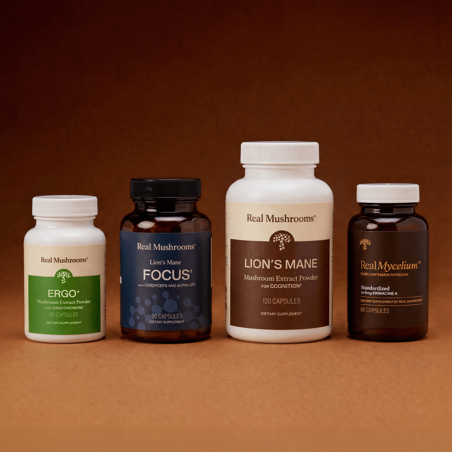 Four bottles of Real Mushrooms supplements—ERGO+, FOCUS, LION’S MANE, and RealMycelium—are arranged side by side against a brown background. The Brain Boosting Bundle from Real Mushrooms is expertly formulated to support cognitive function and brain health.