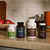 Four bottles from Real Mushrooms’ Brain Boosting Bundle, designed to support brain health and cognitive function, are arranged on a kitchen counter with apples and a ceramic container in the background.