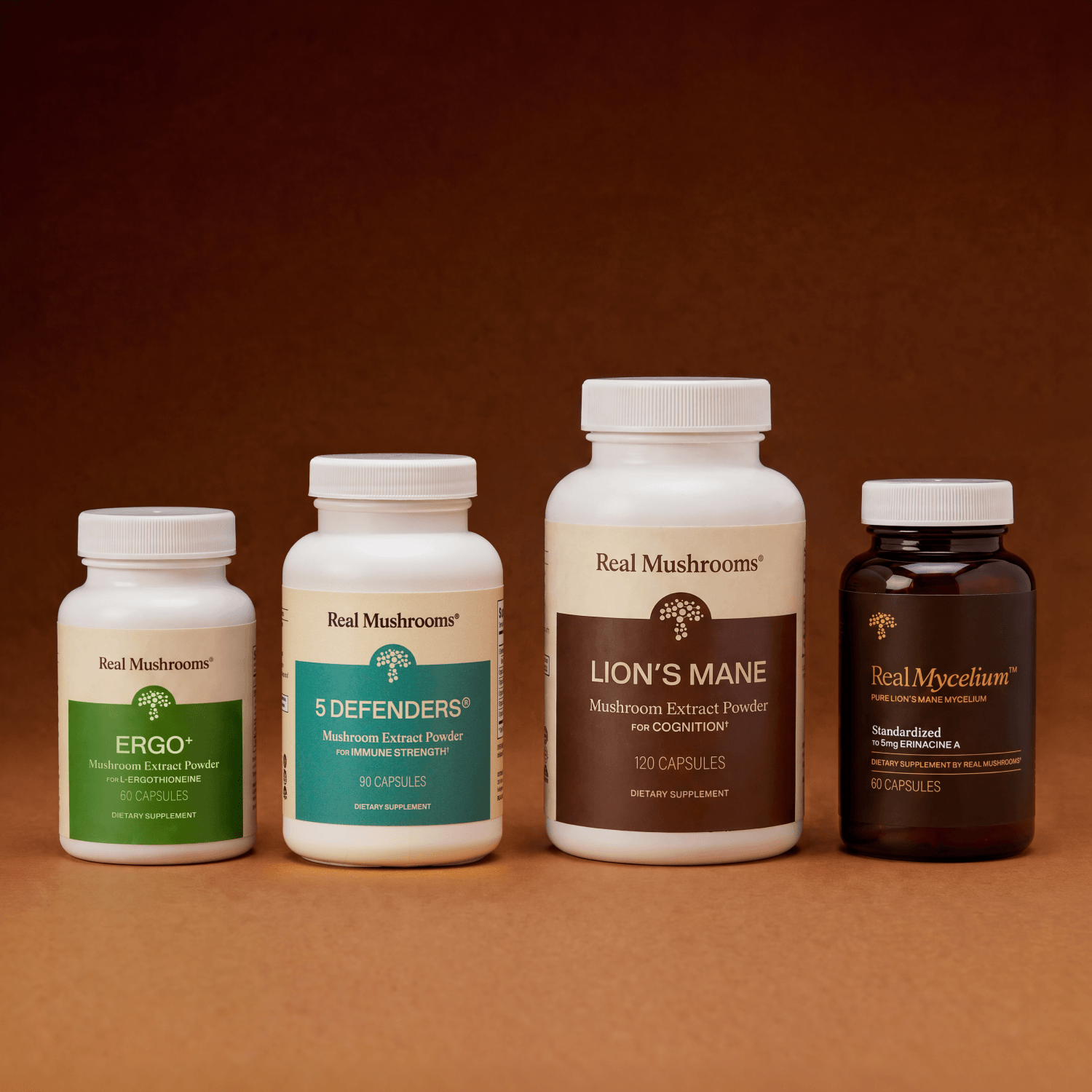 Four supplement bottles from Real Mushrooms’ Complete Mind & Body Bundle—featuring ERGO, 5 Defenders, Lion’s Mane, and Real Mycelium—are arranged in a row against a brown background, highlighting comprehensive mushroom support for brain health and cognitive function.
