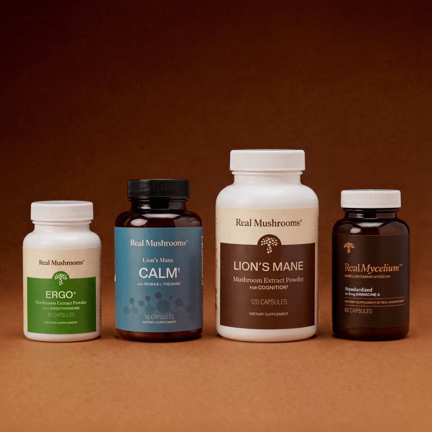 Four Real Mushrooms supplement bottles from the Rest & Restore Bundle are arranged side by side on a brown background, each featuring distinct formulas: Ergo, Calm, Lion’s Mane, and Mycelium. Specially curated by Real Mushrooms, this bundle supports brain health and mood for your daily wellness routine.