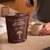 A person froths a cup of Calm Ritual Duo mushroom hot chocolate next to a standing pouch labeled “Real Mushrooms” on a kitchen counter.