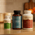 Three bottles of Real Mushrooms’ Daily Calm Trio are displayed on a kitchen counter with fruit and kitchen items in the background.
