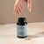 A hand reaches for a capsule beside an open Real Mushrooms Daily Calm Trio bottle on a light surface.