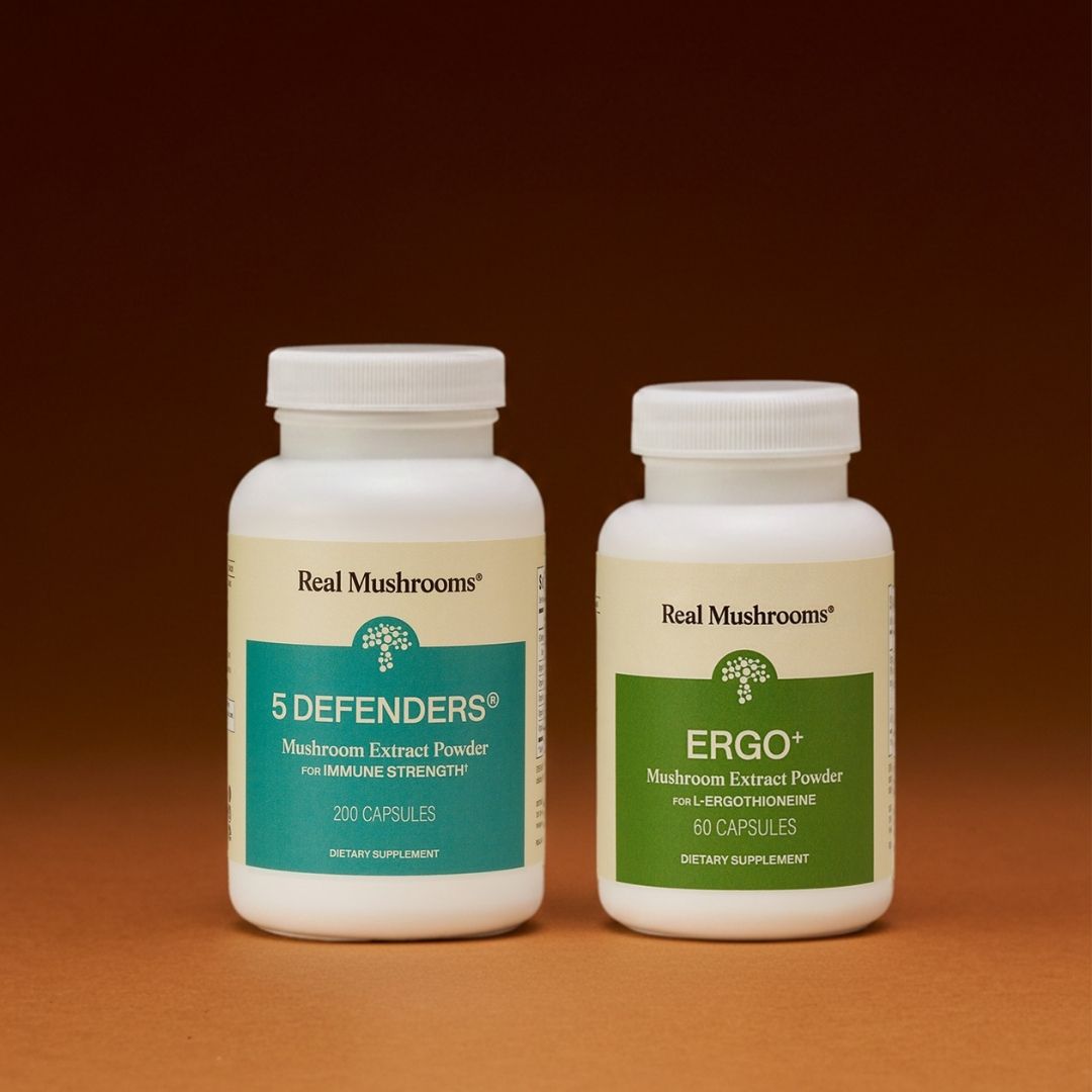 Two white bottles of Real Mushrooms Immune Power supplements are displayed side by side against a brown background, highlighting their mushroom formulation known for beta-glucans and immune support.