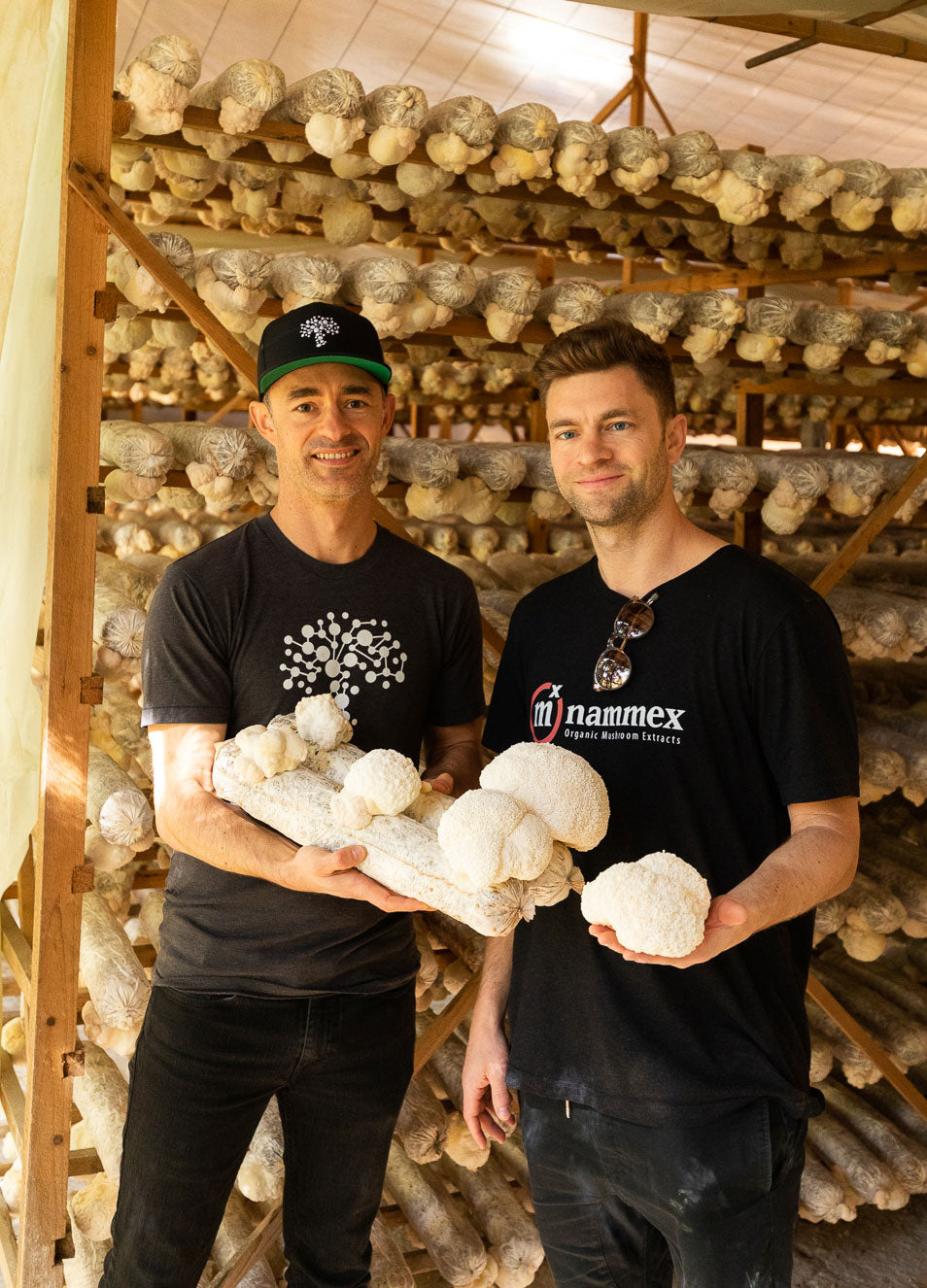 Adam and Skye Chilton holding large white mushrooms in a mushroom cultivation facility.