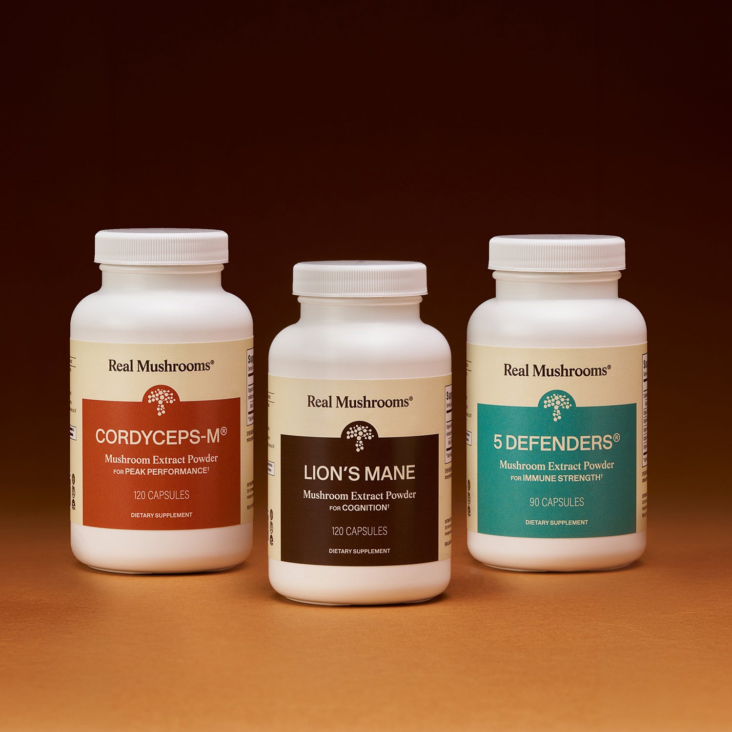 Real Mushrooms’ The Big 3 supplements are shown side by side on a brown surface with a gradient background, highlighting their mushroom extracts that support brain health and immune function.