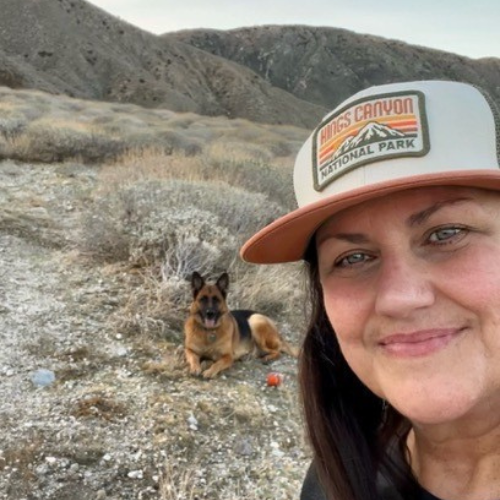 Jill Vega wearing a cap with  National Park logo and a dog sitting on a rocky landscape.