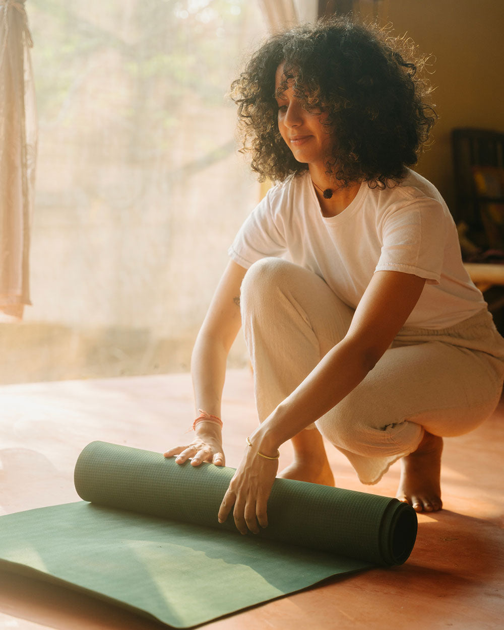 Person rolling up a green yoga mat in a bright room with natural light.