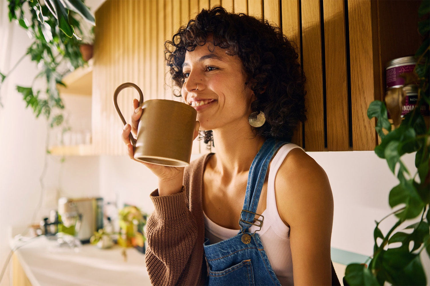 Woman holding a mug in a kitchen with plants and shelves in the background