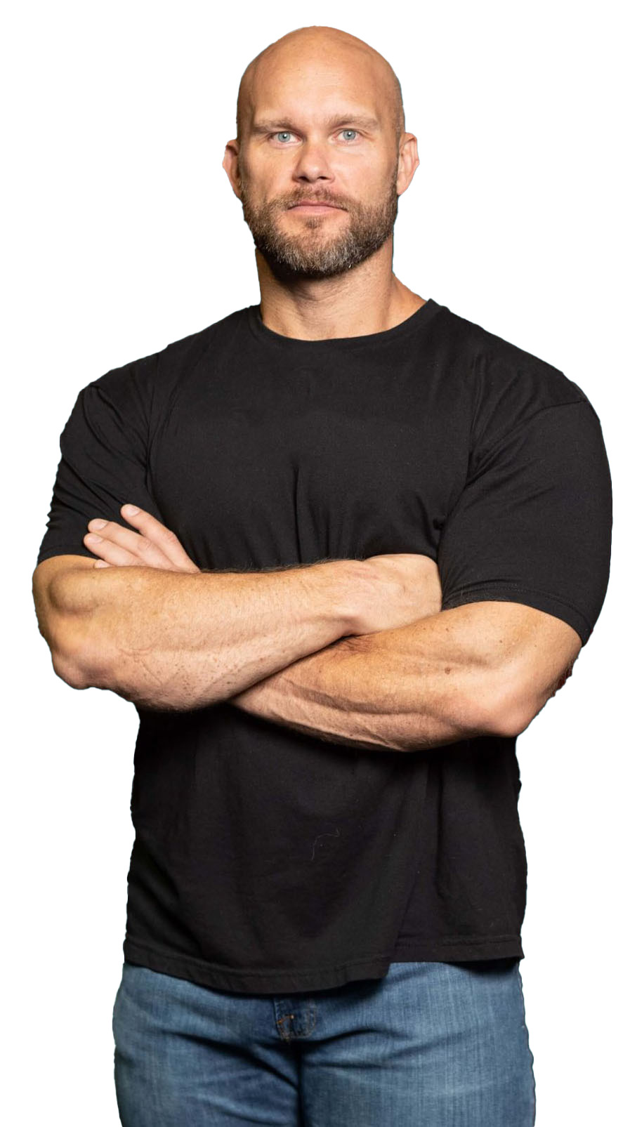 A person with a bald head, beard, and muscular build crosses their arms while wearing a black T-shirt and blue jeans.