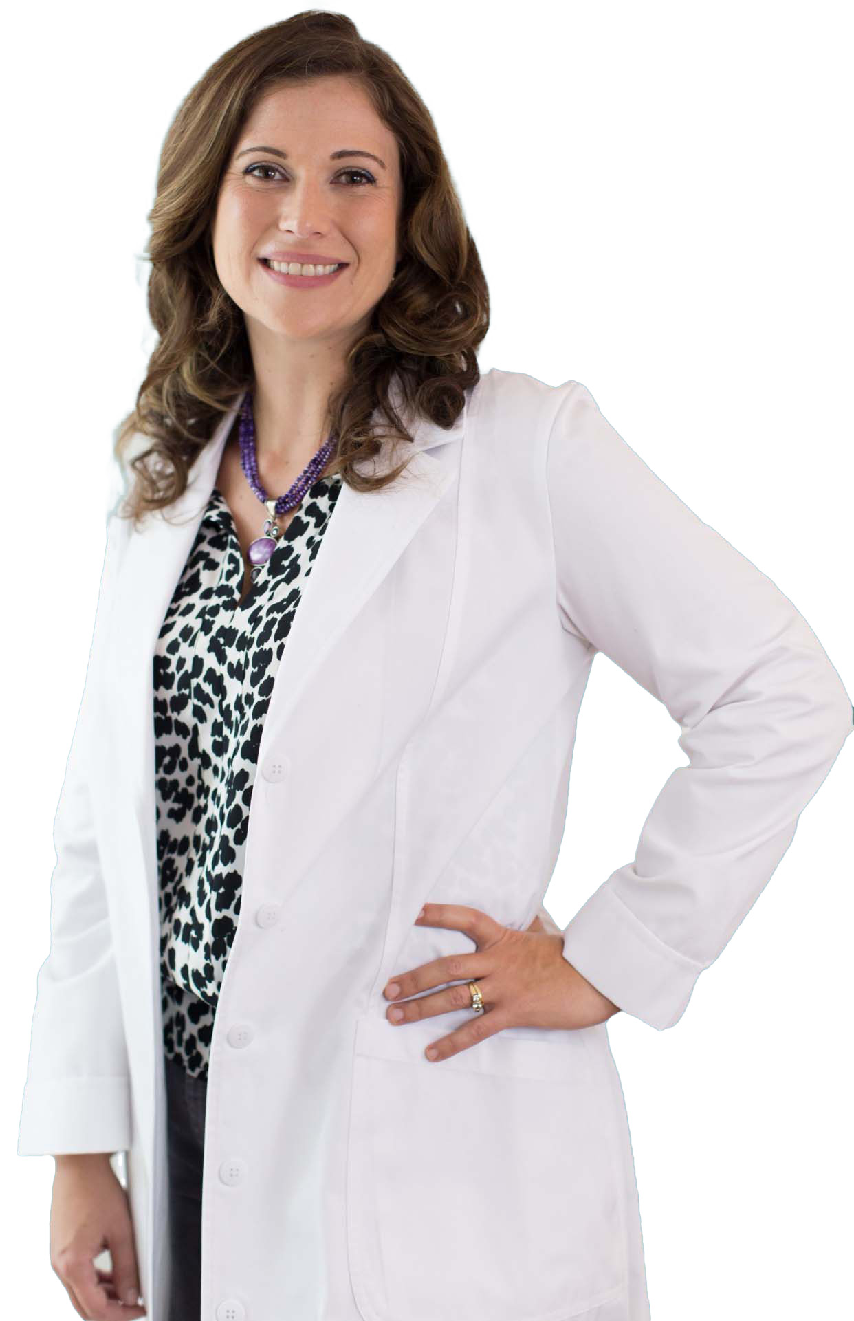 A person with shoulder-length brown hair and a smile, wearing a white lab coat over a patterned blouse, stands with one hand on their hip.