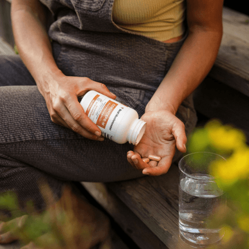 woman holding a cordyceps mushroom supplement bottle and its capsules on her other hand