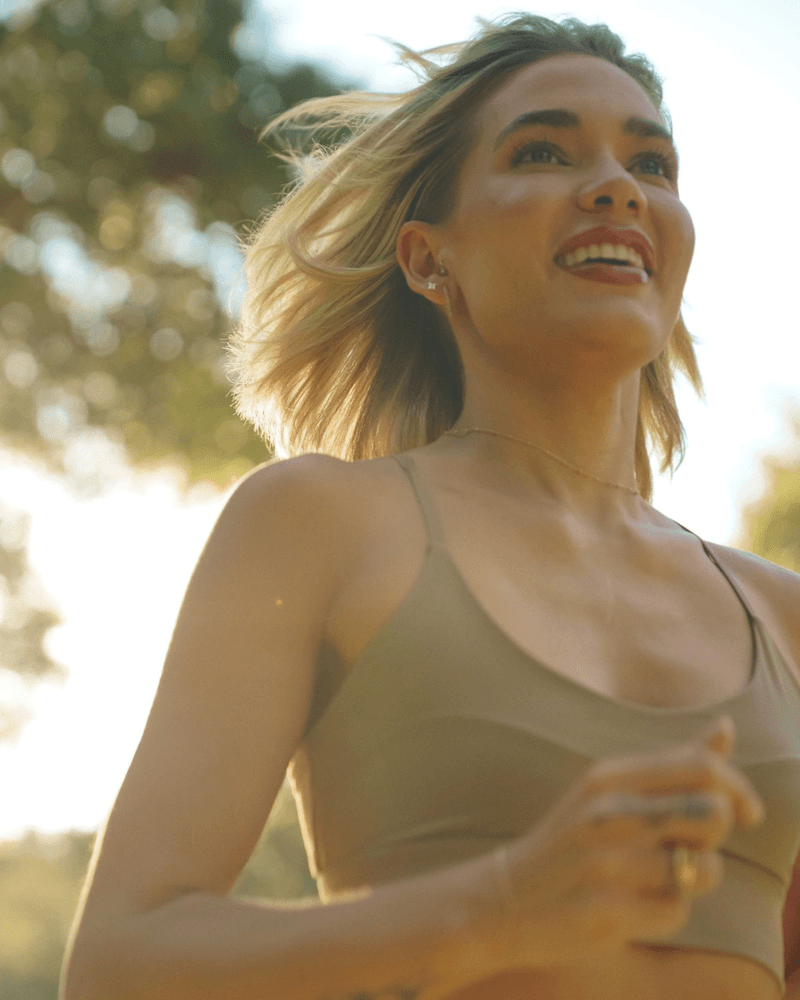 Woman running and smiling with tree leaves in the background
